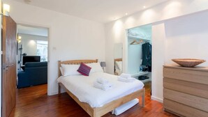 A modern bedroom with a wooden bed, white linens, a wooden dresser, and a mirror.