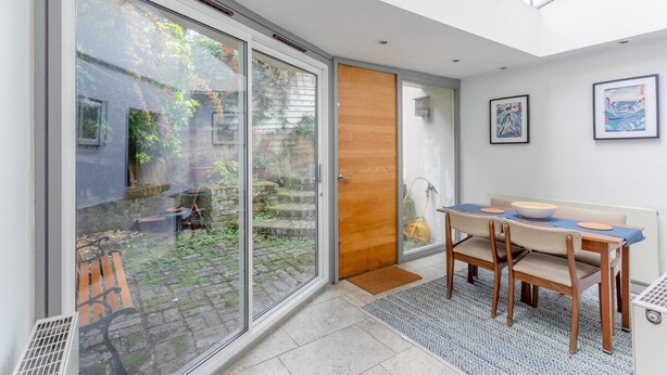 A modern interior with a dining area, a sliding glass door leading to a garden, and artwork on the walls.