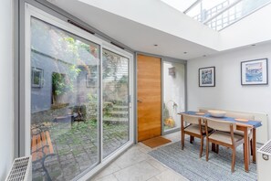 A modern interior with a dining area, a sliding glass door leading to a garden, and artwork on the walls. - Fantastic and Bright 1 Bedroom Garden Flat (London)