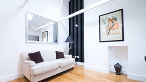 A modern living room with a white sofa, a large mirror, a framed artwork, and a floor lamp. - Contemporary 1 Bedroom Flat in Fulham near The Thames (London)