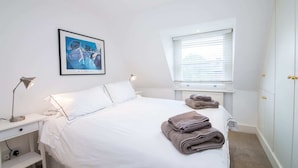 A bedroom with a bed, a desk, a lamp, a framed picture, a window, and a wardrobe. - Contemporary 1 Bedroom Flat in Fulham near The Thames (London)