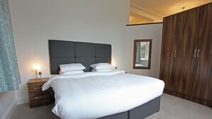 Une chambre à coucher moderne avec un grand lit, une armoire en bois et une table de chevet avec une lampe.