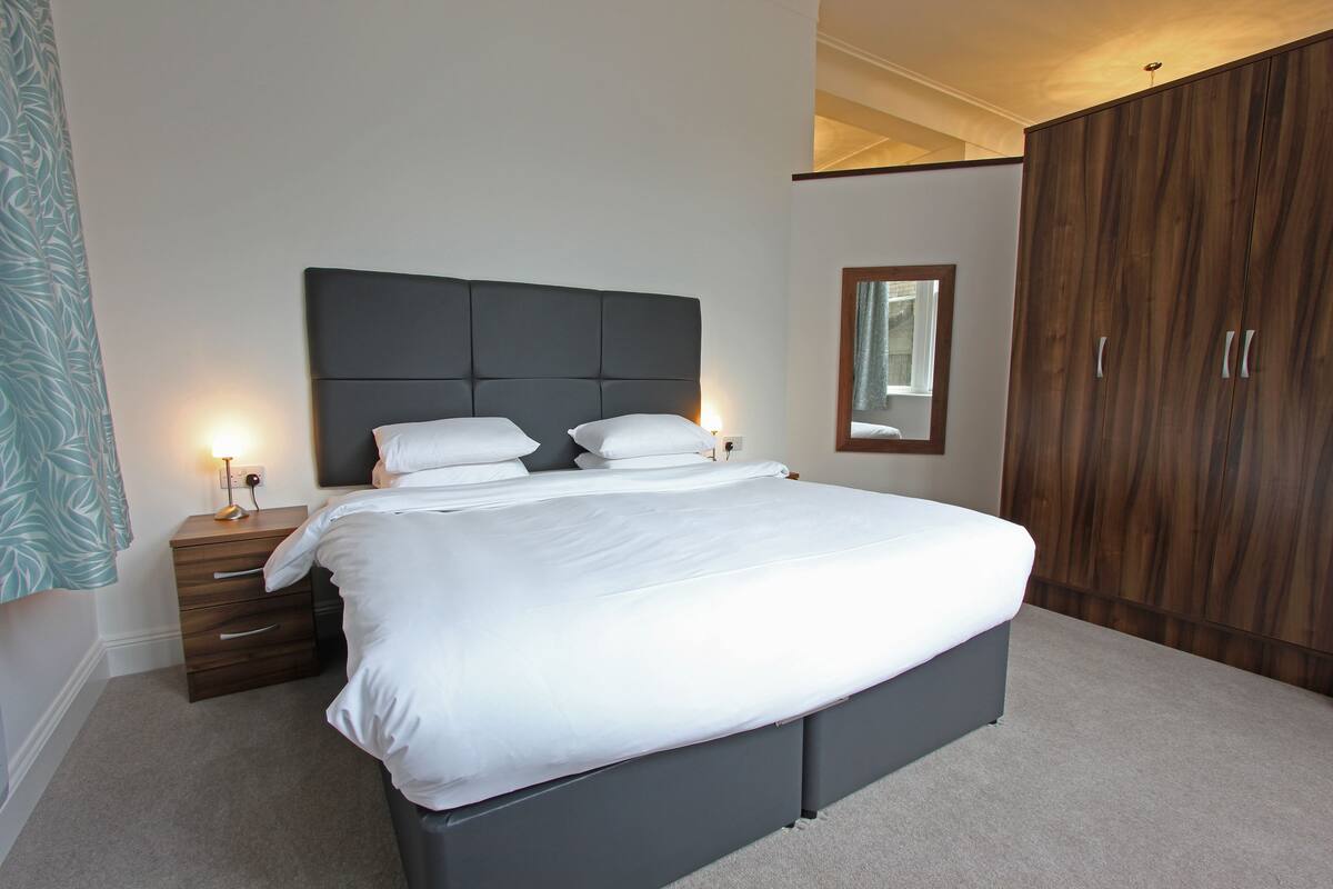 A modern bedroom with a large bed, a wooden wardrobe, and a bedside table with a lamp.