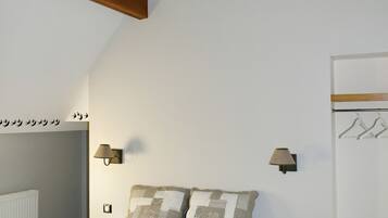 Une chambre à coucher avec un lit, des poutres en bois, un luminaire fixé au mur, un radiateur, une table de chevet, un banc et un porte-manteau.