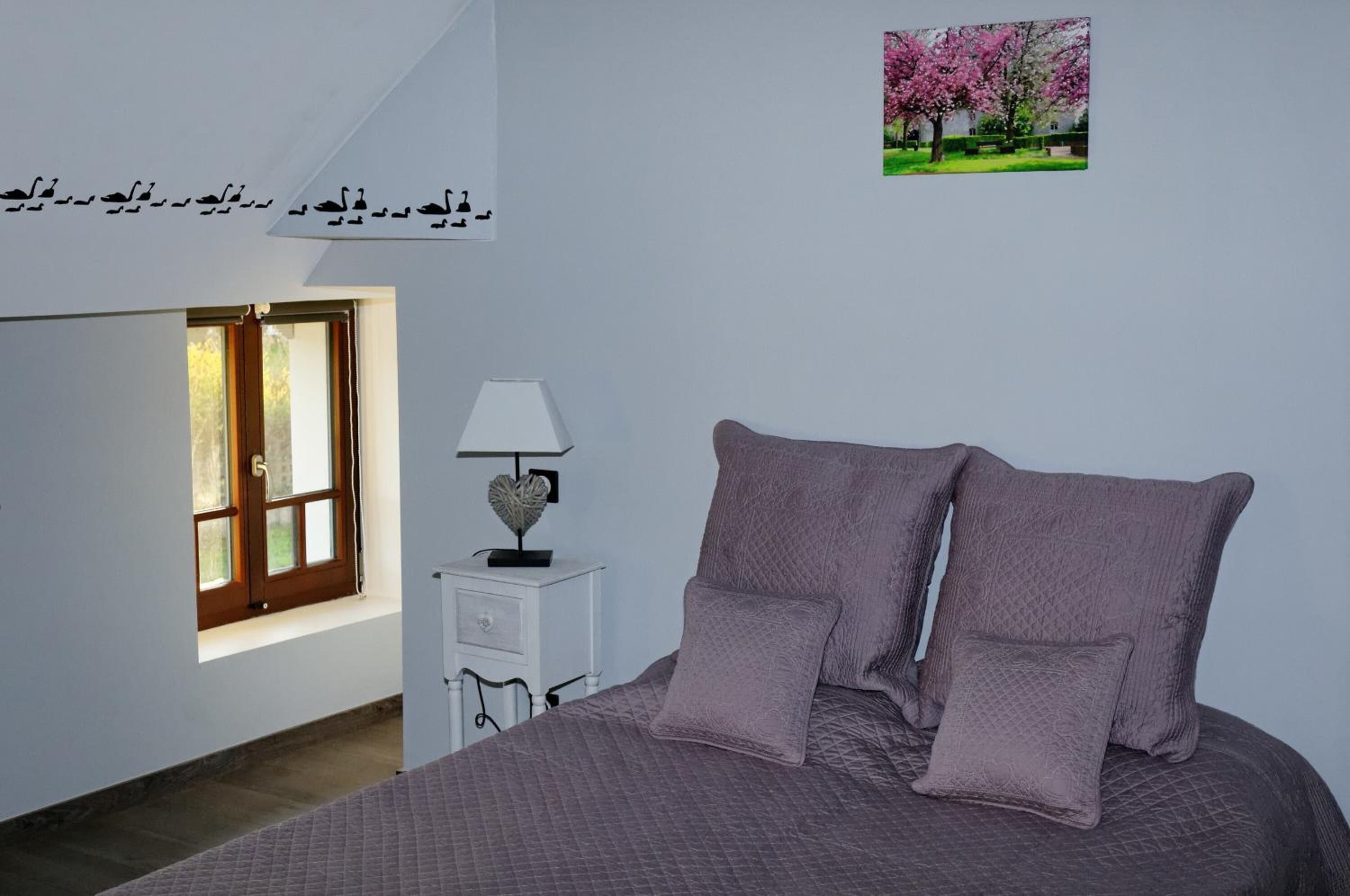 Une chambre à coucher comprenant un lit, une table de chevet, une lampe, une fenêtre et un élément de décoration murale.