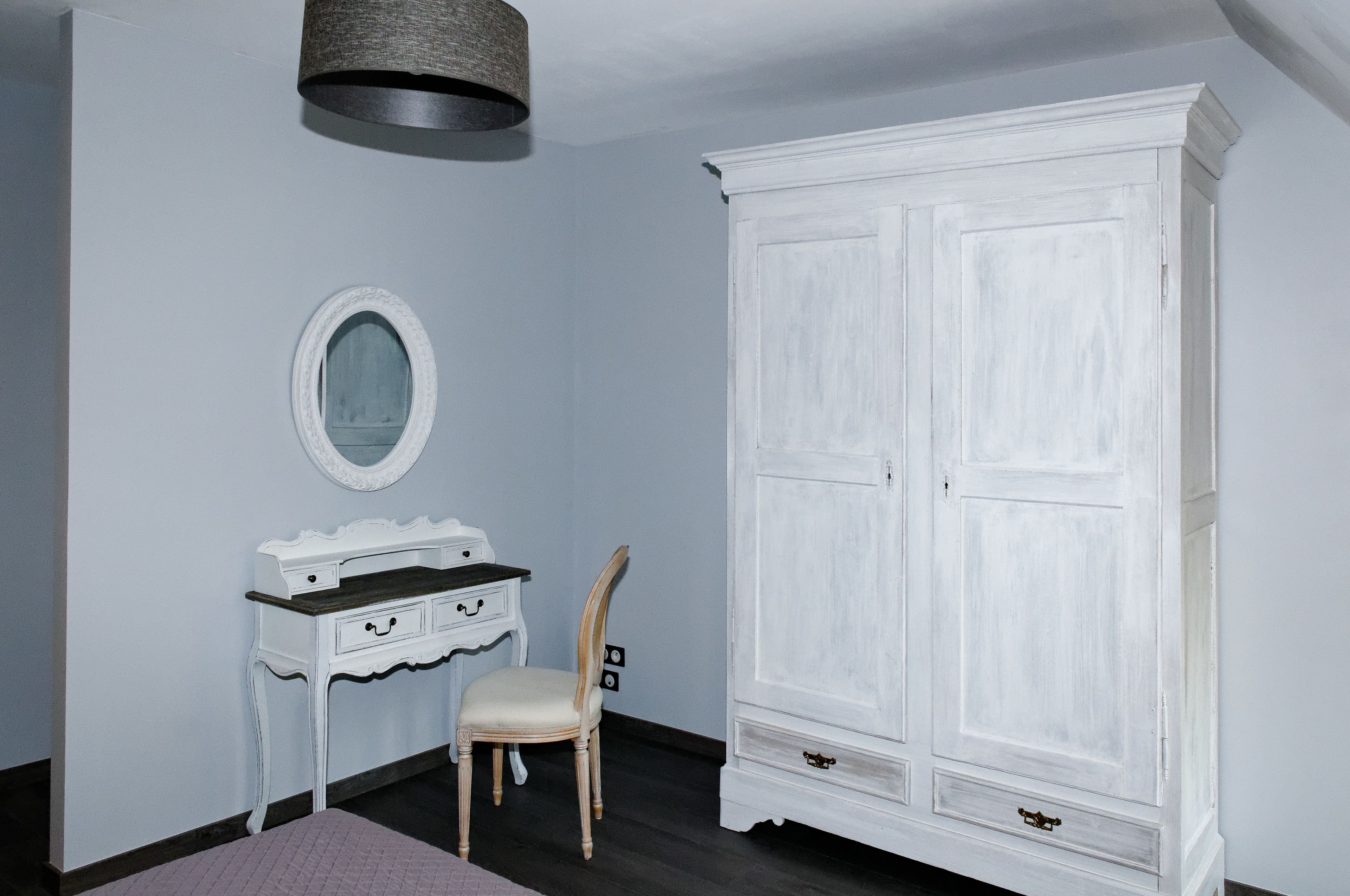A room with a white wardrobe, a vanity with a mirror, and a chair.