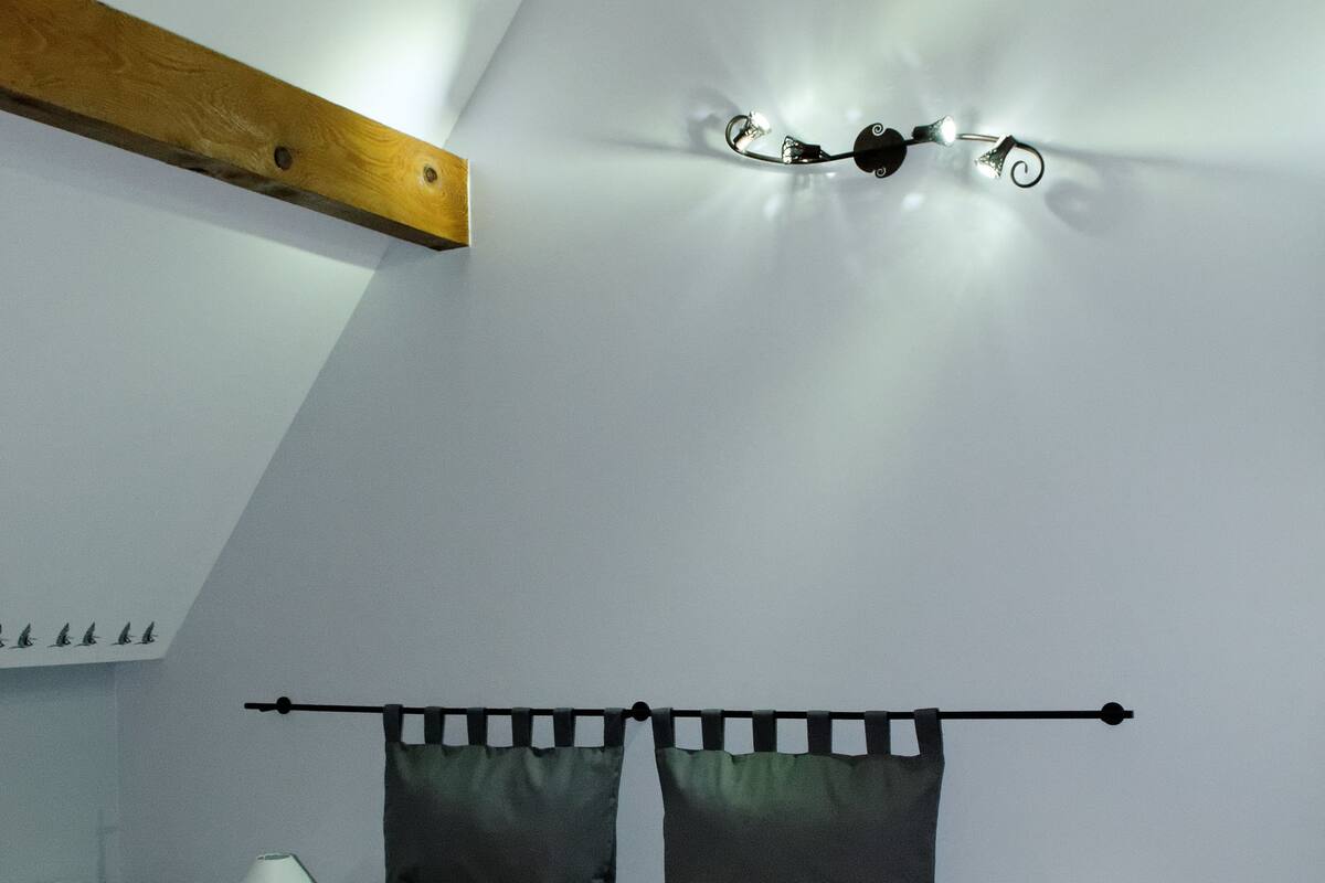 A bedroom with a sloped ceiling, a bed with a headboard, two bedside tables with lamps, and a wall-mounted light fixture.