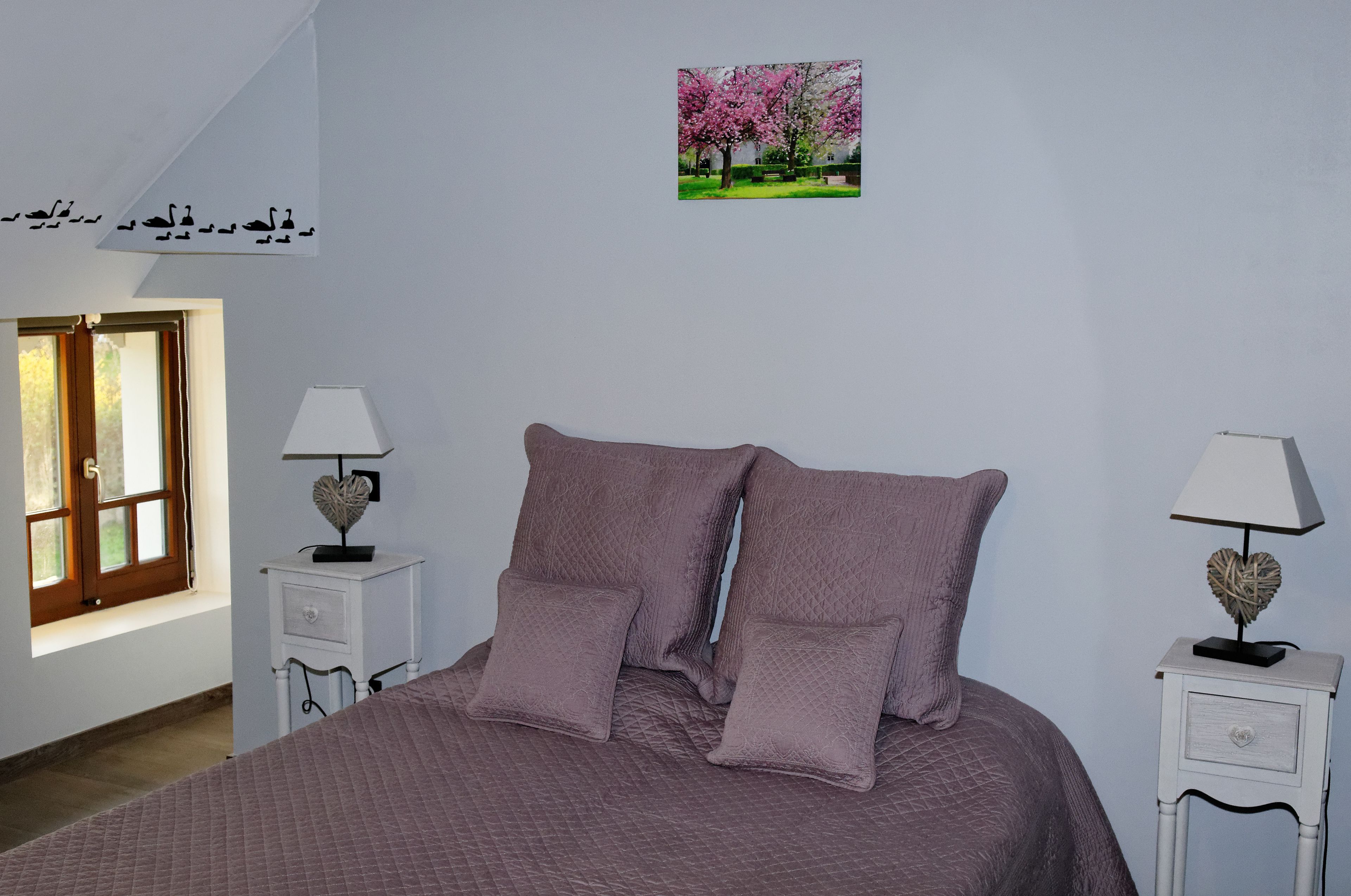 Une chambre à coucher avec un lit, deux tables de chevet, une fenêtre et un tableau au mur.