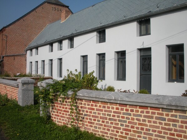A white building with multiple windows and a brick wall. - La Ferme Aux Charmes (Solre-le-Château)