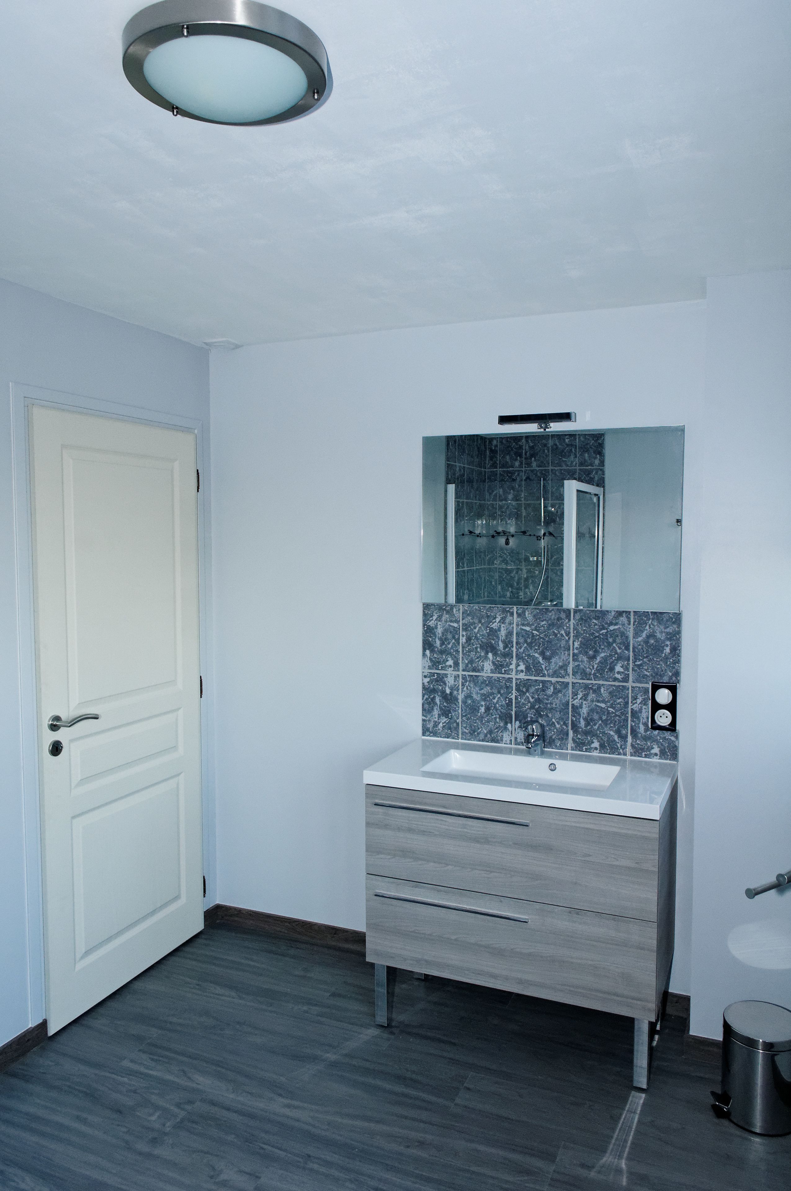 A bathroom with a white door, a sink with a mirror above it, and a tiled backsplash.