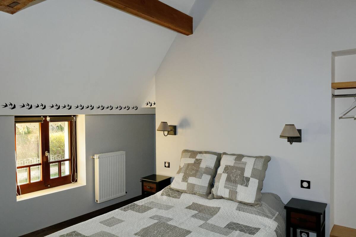 A bedroom with a bed, a window with a view, a radiator, and two wall-mounted lamps.