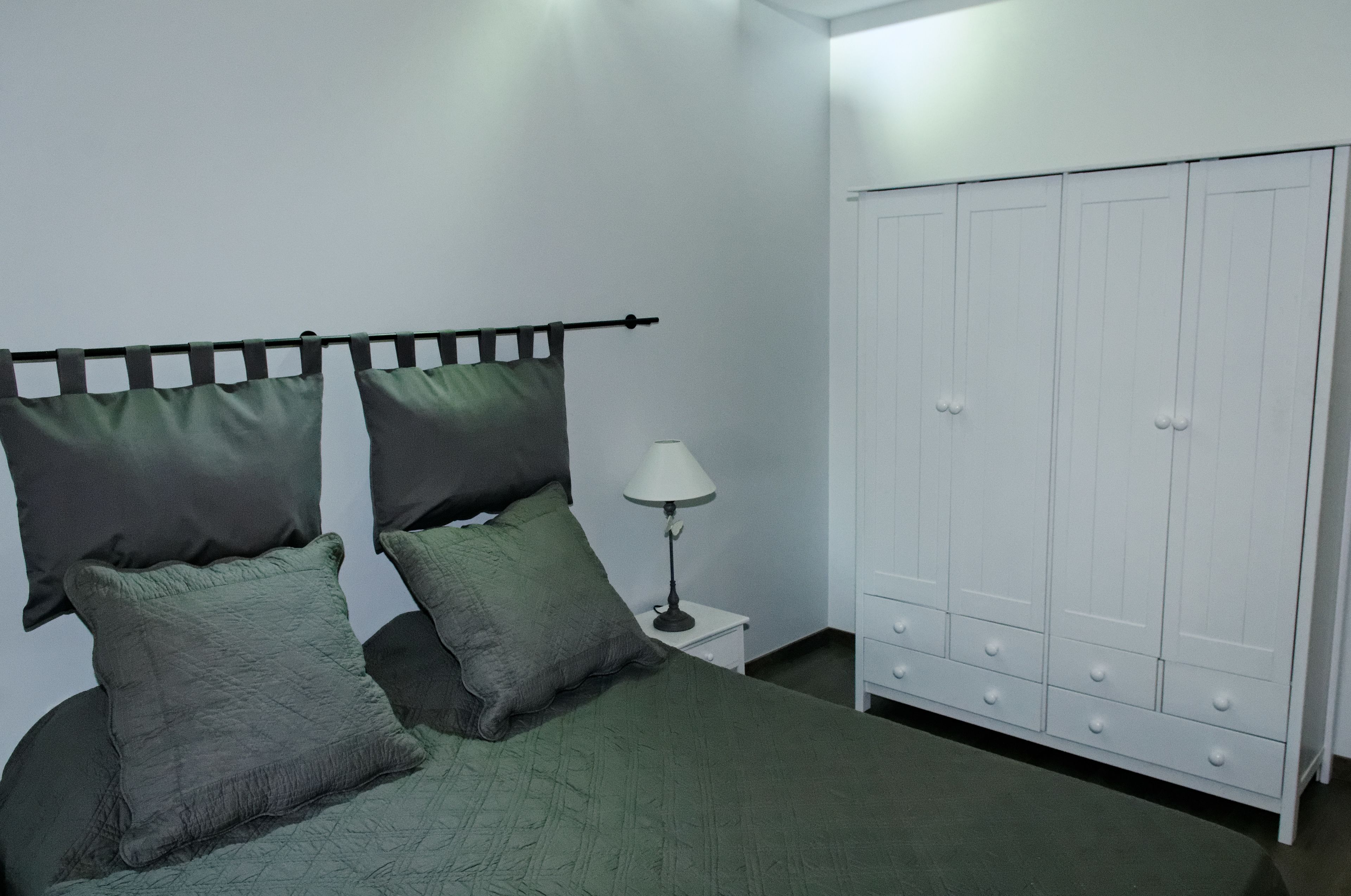 Ein Schlafzimmer mit einem Bett, grüner Bettwäsche, einem Nachttisch mit Lampe und einem weißen Kleiderschrank.
