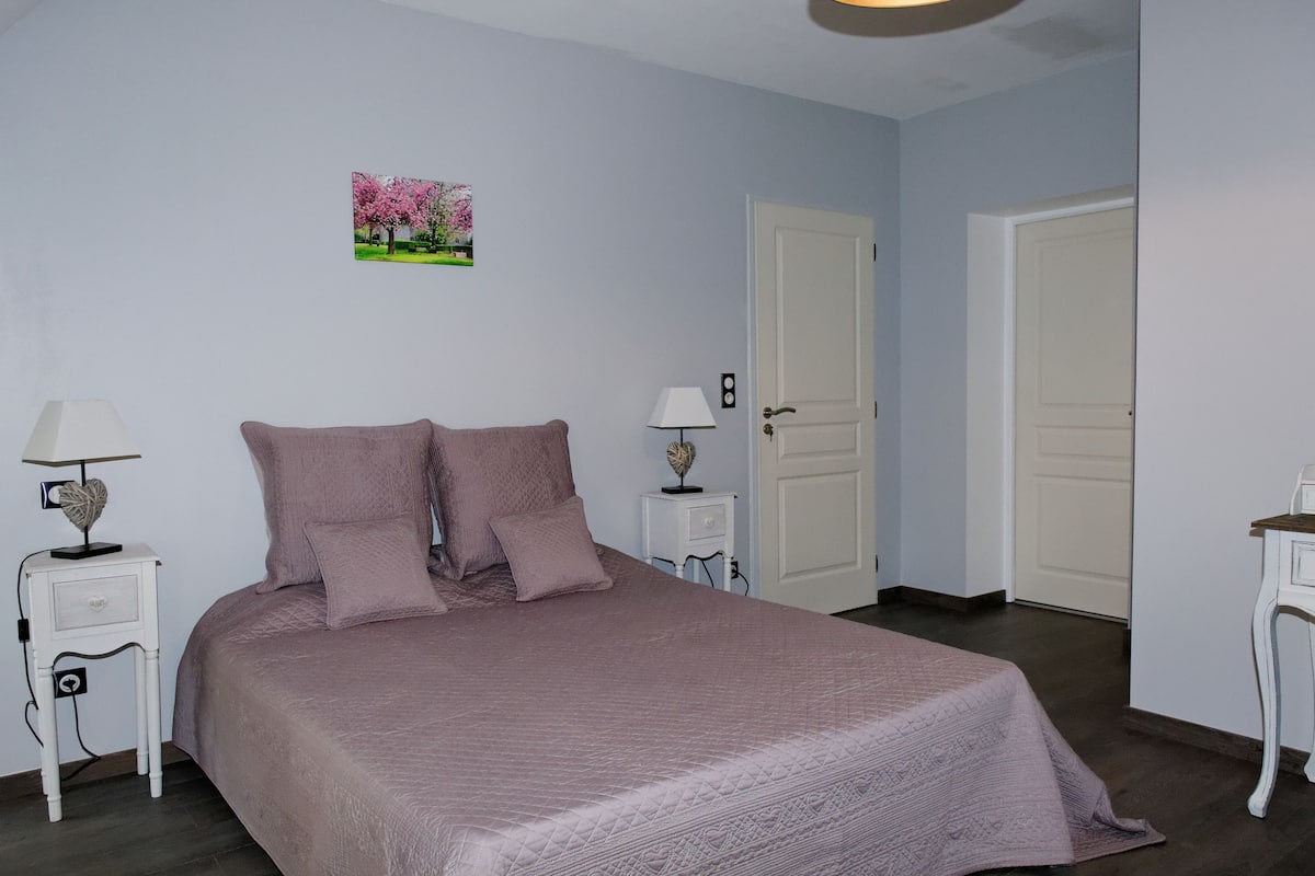 A bedroom with a large bed, two bedside tables with lamps, a picture on the wall, and two doors.