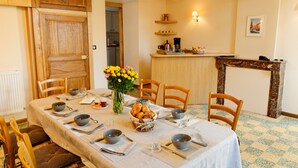 A dining area with a table set for six, wooden chairs, a vase with flowers, and a kitchen in the background. - La Ferme Aux Charmes (Solre-le-Château)