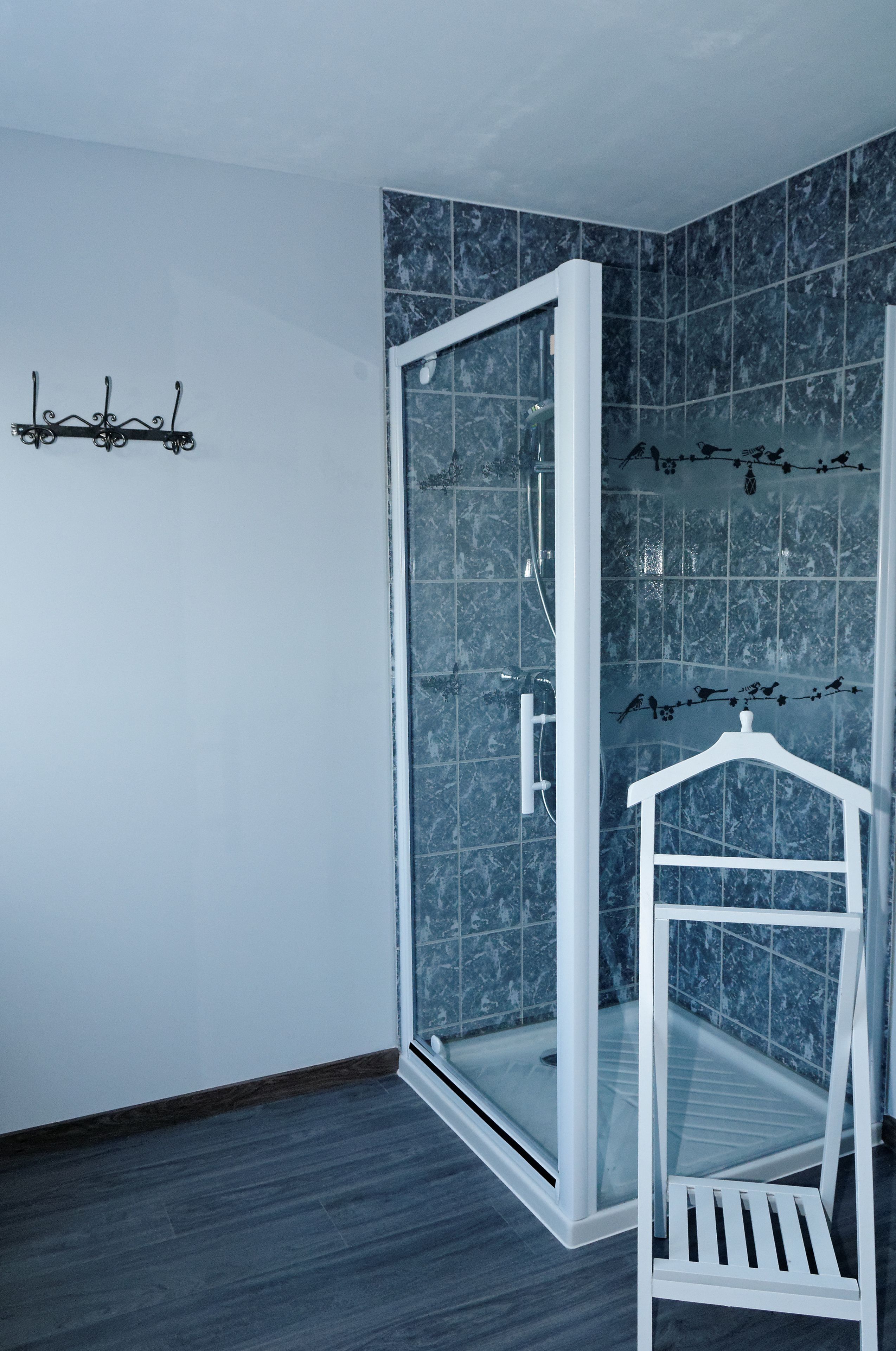 Une salle de bain d’angle avec une douche à parois de verre, un banc blanc et un porte-serviettes mural.