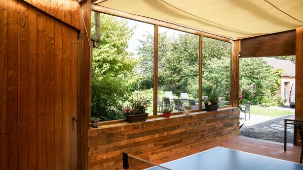 A ping pong table in a wooden room with a large window overlooking a garden. - La Ferme Aux Charmes (Solre-le-Château)