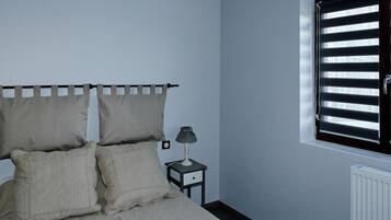 A bedroom with a bed, a nightstand with a lamp, and a window with blinds.