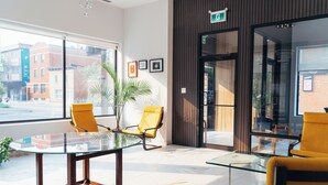 A modern interior with a glass table, yellow chairs, a potted plant, and large windows offering a city view. - Cjour Apartments (Montreal)