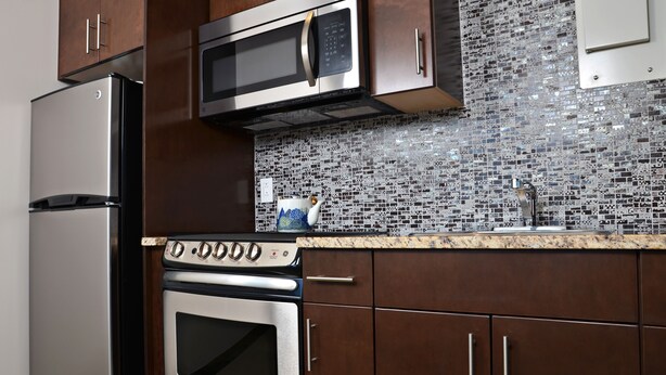A kitchen with stainless steel appliances, a tiled backsplash, and wooden cabinets. - Cjour Apartments (Montreal)