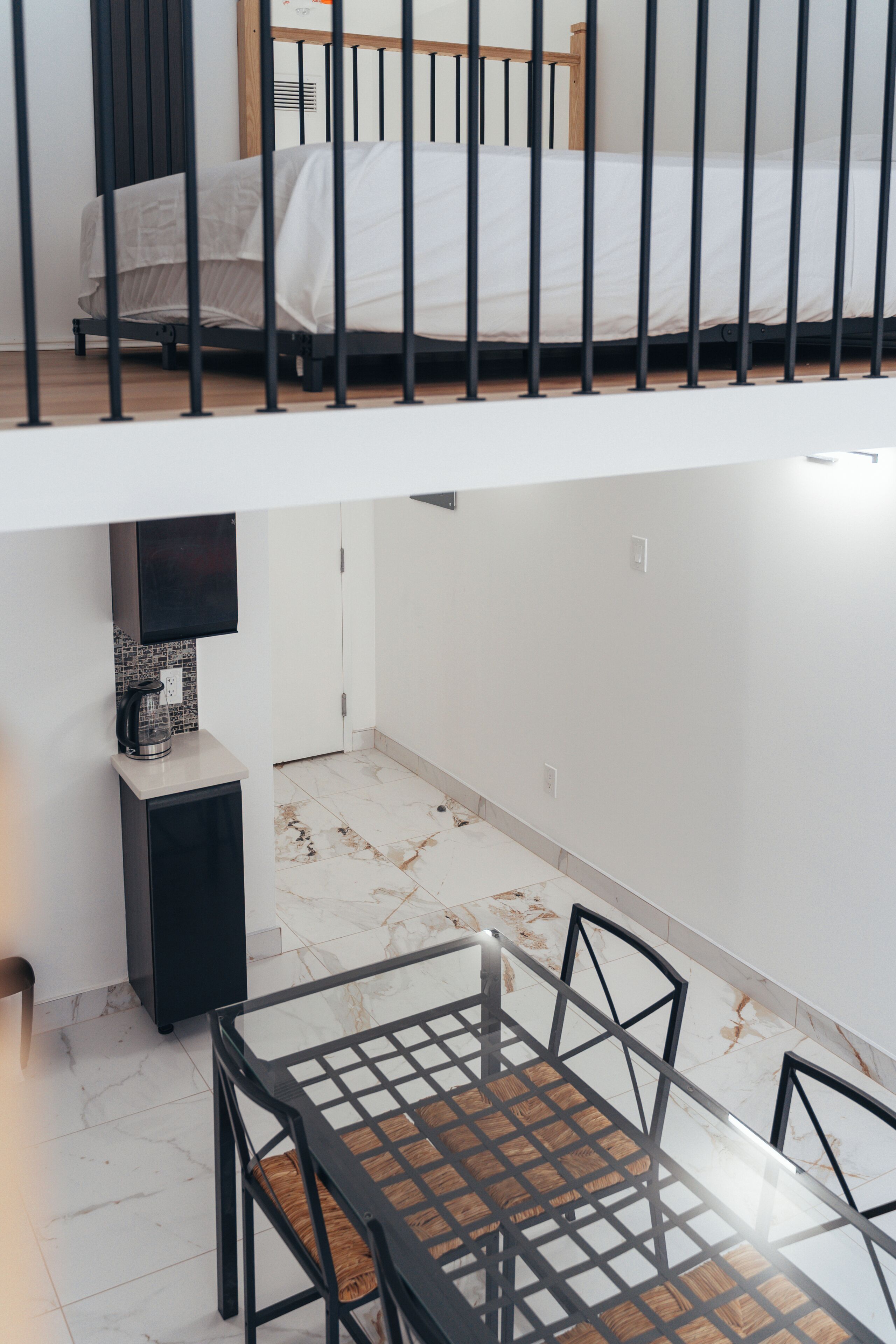 A modern room with a bed, a TV mounted on the wall, a small table with chairs, and a tiled floor.