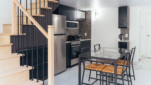 A modern kitchen with a glass dining table, black chairs, a built-in oven, and a stainless steel refrigerator. - Cjour Apartments (Montreal)
