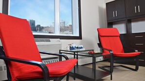 A modern kitchen with two red chairs, a small table, and a window with a city view. - Cjour Apartments (Montreal)
