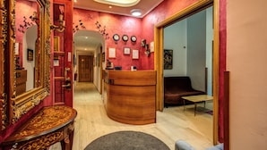 Un área de recepción con un mostrador de madera, un espejo grande y una pared roja con relojes y certificados.