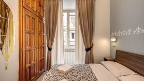 Un dormitorio con un amplio armario de madera, una colcha estampada y vistas a través de una ventana con cortinas.