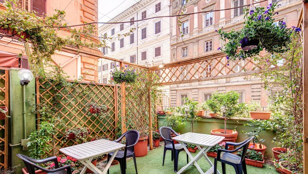 Un pequeño patio al aire libre con una mesa y sillas, rodeado de macetas con plantas y una cerca de listones de madera.