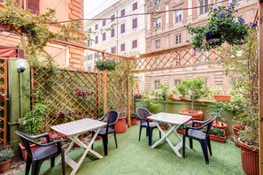 A small outdoor patio with a table and chairs, surrounded by potted plants and a wooden lattice fence. - Hotel Orbis (Rome)