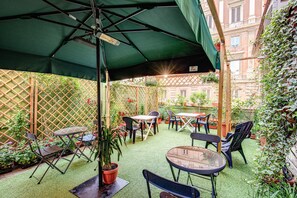 An outdoor patio with tables and chairs, surrounded by potted plants and a wooden fence. - Hotel Orbis (Rome)