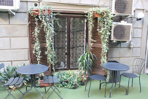 A patio with two round tables and four chairs, surrounded by potted plants and a decorative iron gate. - Hotel Orbis (Rome)
