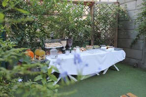 An outdoor dining area with a table set for a meal, surrounded by greenery and a wooden pergola. - Hotel Orbis (Rome)