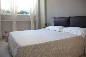 Una cama bien hecha con una colcha estampada, una mesita de noche con lámpara y una ventana con cortinas.
