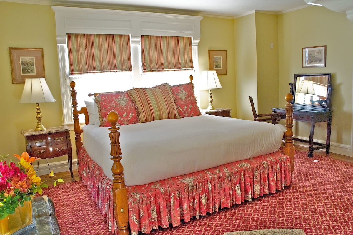 Une chambre à coucher avec un grand lit, deux tables de chevet, une commode, une chaise et un miroir.