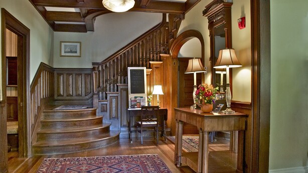 A grand staircase with wooden railings and a patterned rug leading to a dining area with a table and chairs. - Hilltop Inn (Newport)