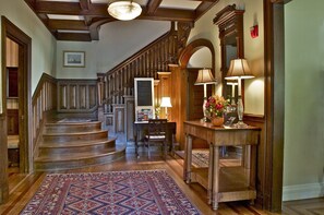 Un magnifique escalier en bois, doté de rampes et surmonté d’un tapis à motifs, mène à un espace repas comprenant une table et des chaises.