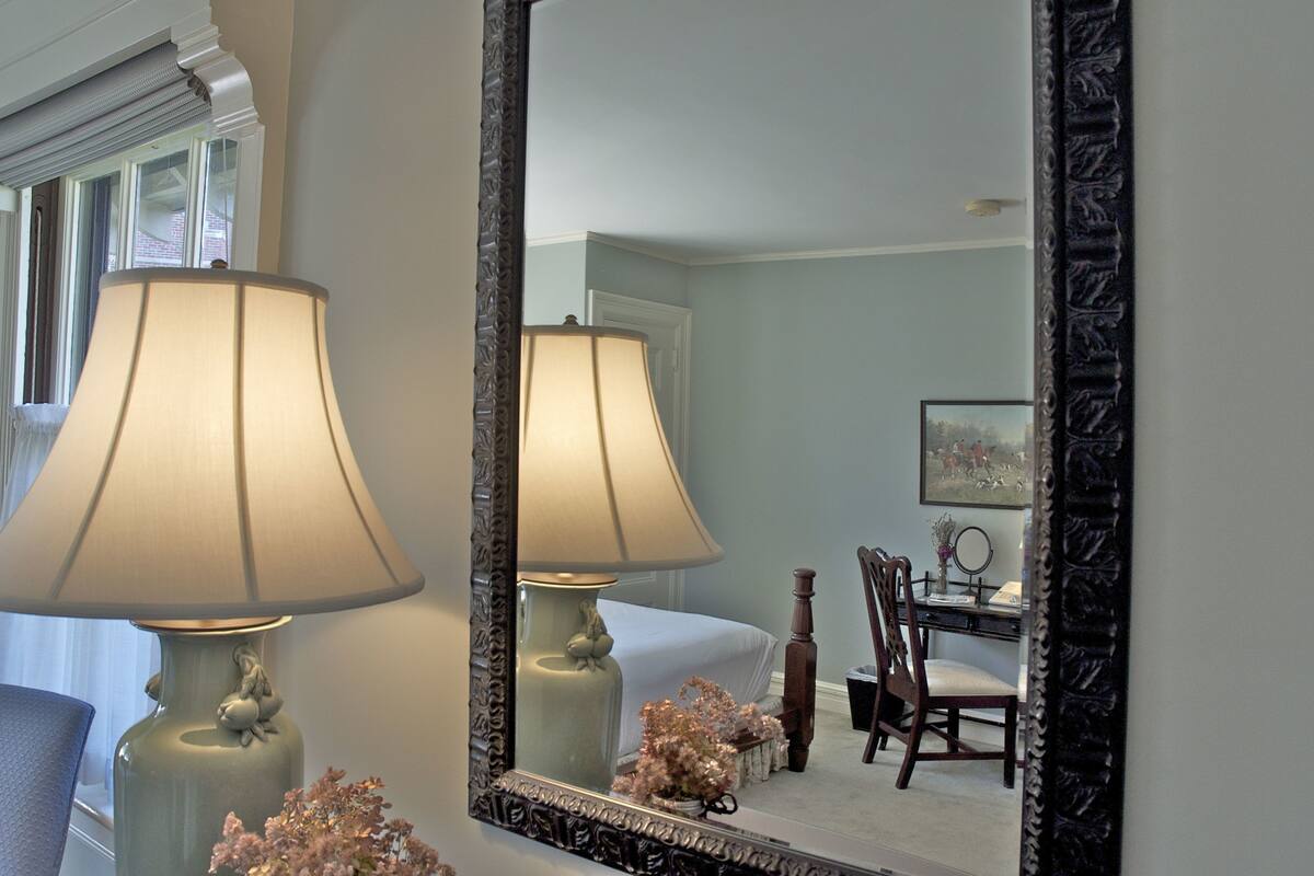 Une chambre comprenant un lit, un bureau avec une chaise et un miroir doté d’un cadre décoratif.