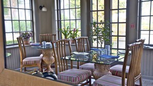 A dining area with a glass table, striped cushioned chairs, and potted plants. - Hilltop Inn (Newport)