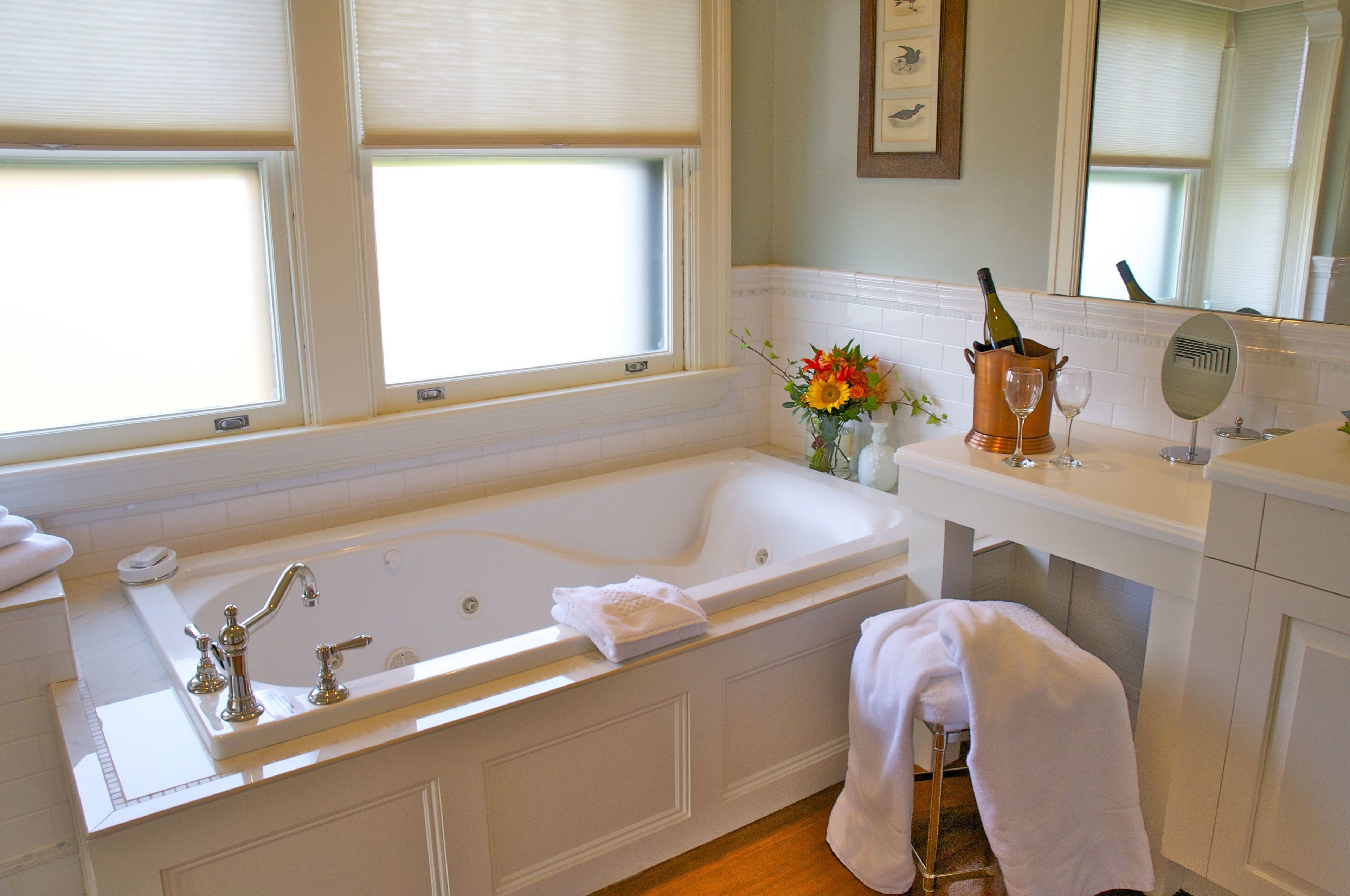 A bathroom with a large bathtub, a vanity with a mirror, and a window with blinds.