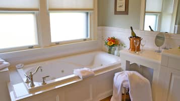 A bathroom with a large bathtub, a vanity with a mirror, and a window with blinds.
