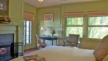 A room with a fireplace, a desk with a lamp, a chair, and a bed.