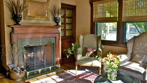 A living room with a fireplace, a sofa, a chair, and a window with blinds. - Hilltop Inn (Newport)