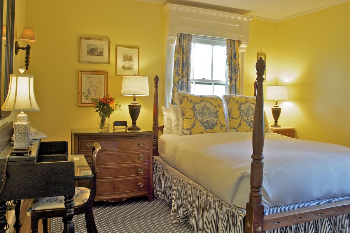 Une chambre à coucher avec un lit à baldaquin, une commode, un bureau avec une chaise et une fenêtre avec des rideaux.