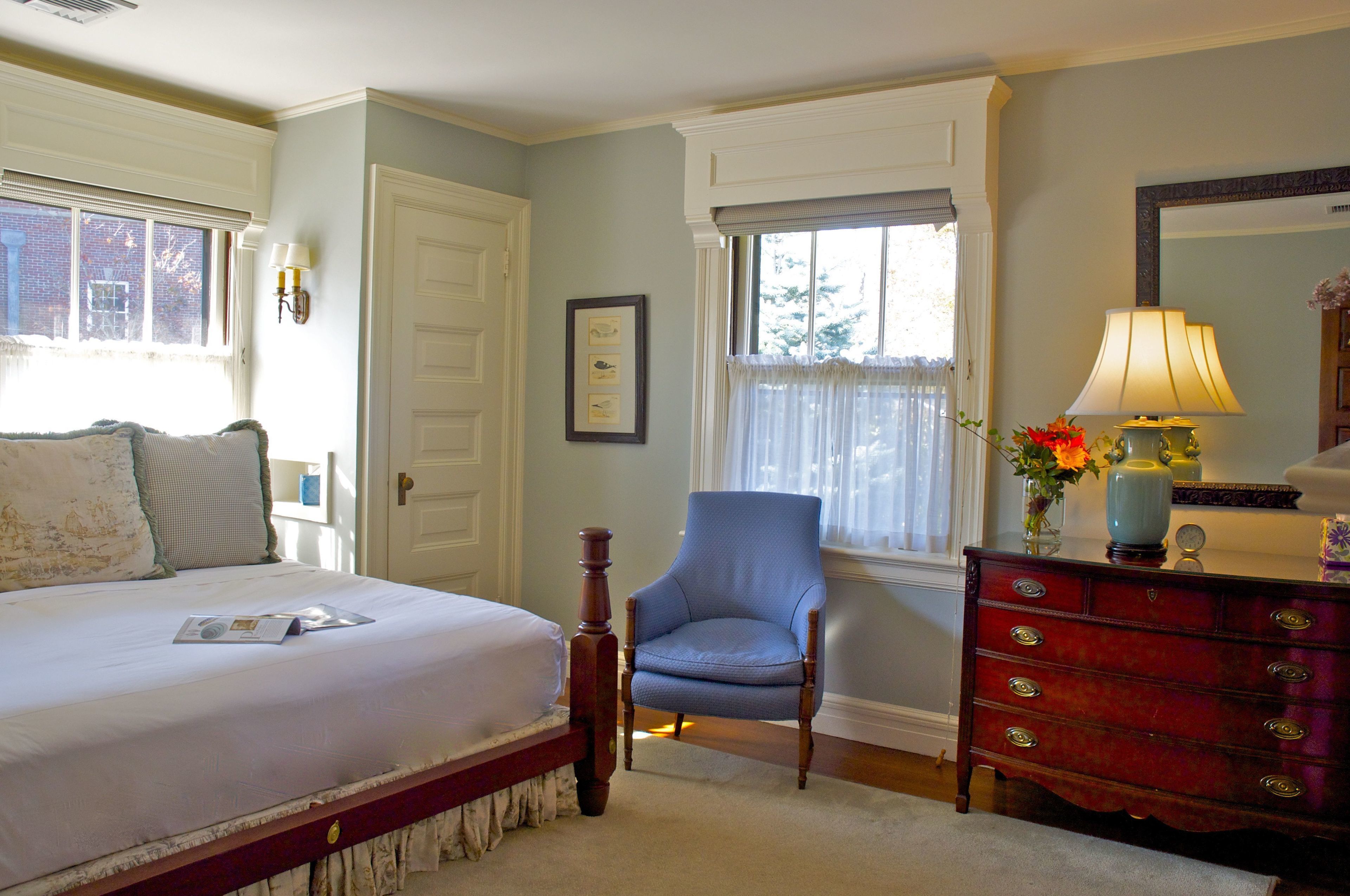 A bedroom with a bed, a chair, a dresser, and a window with a view of the outside.