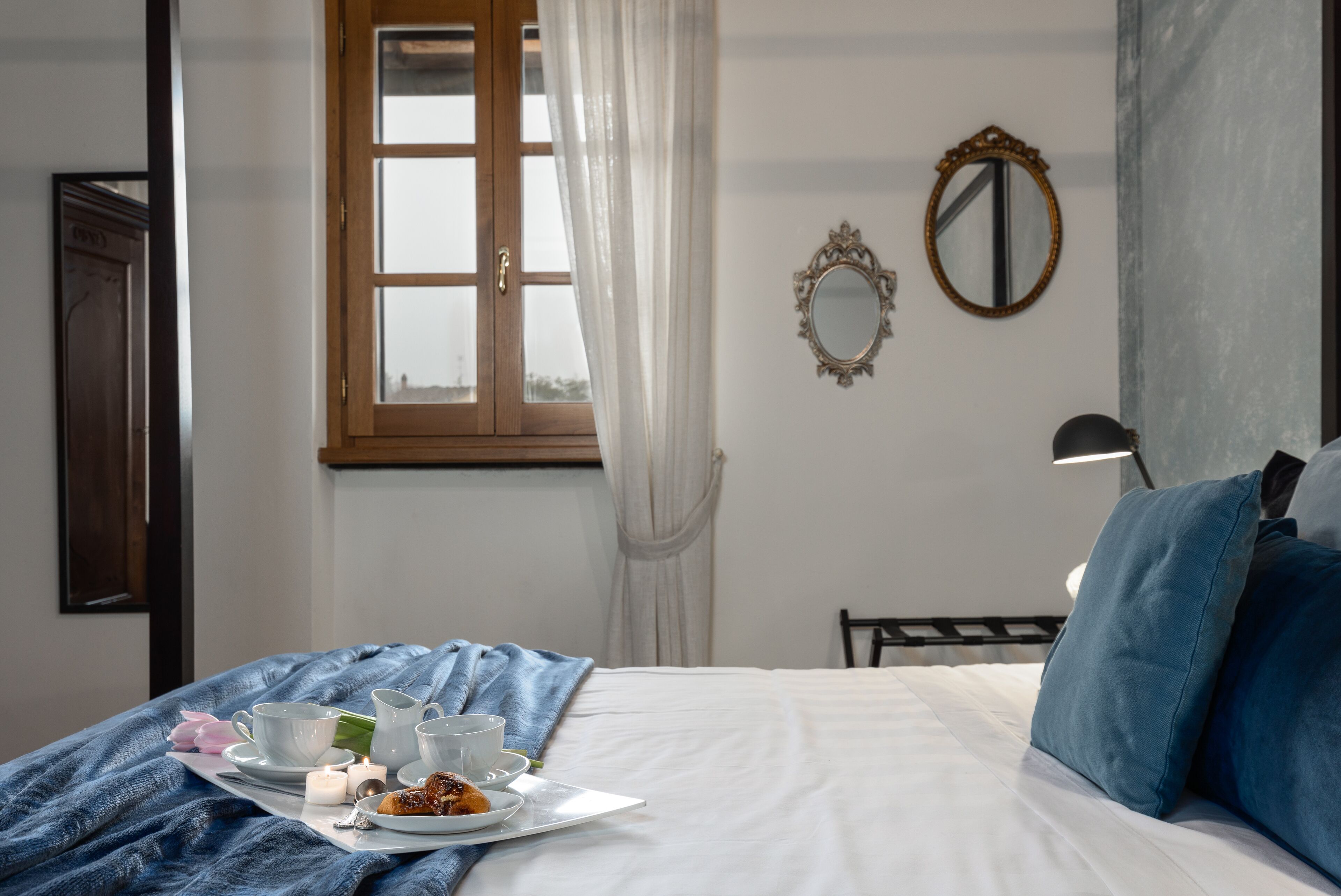 Un llit ben arropat amb una bandeja de menjars, una finestra amb cortines i un mirall a la paret.