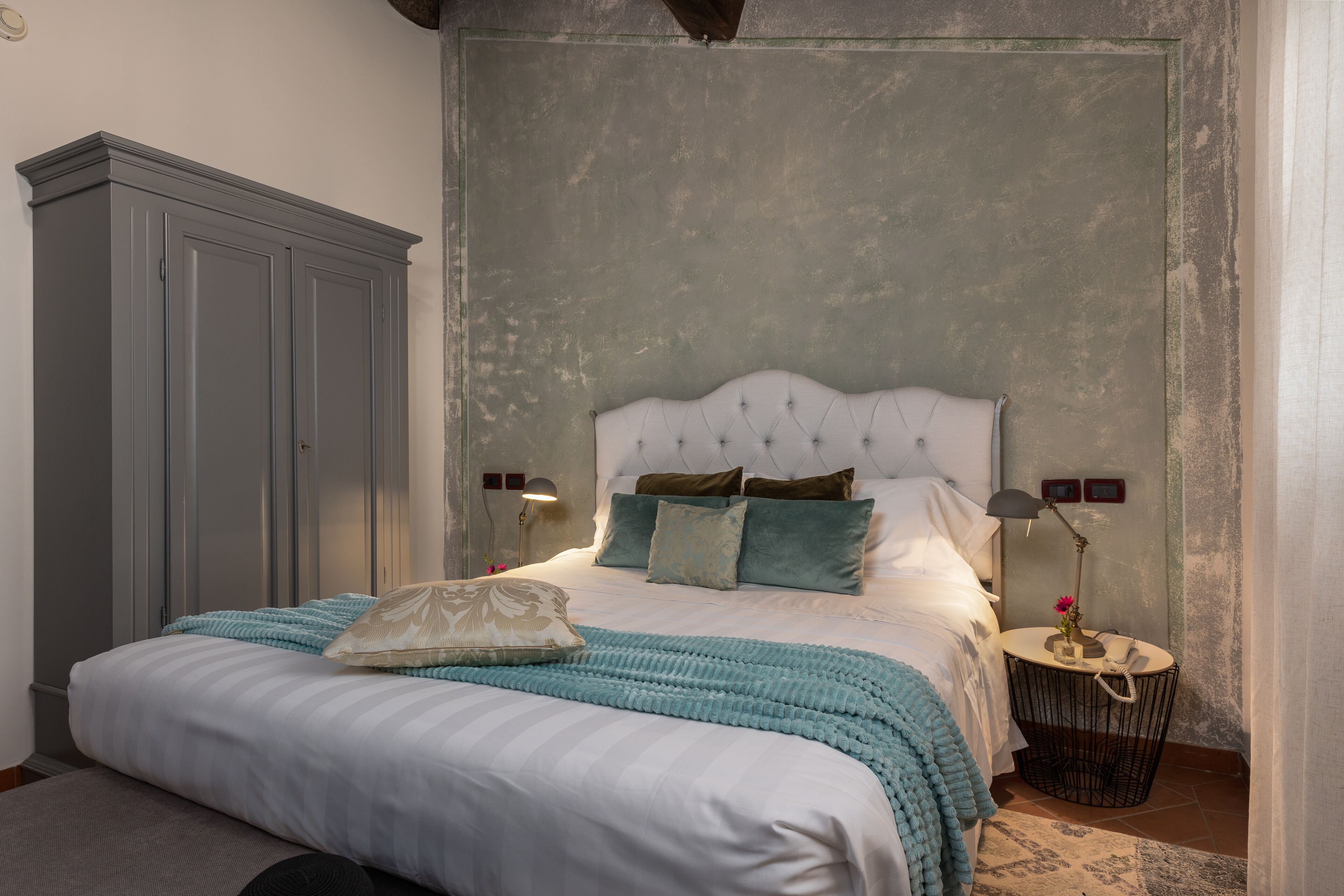 A bedroom with a large bed, a wardrobe, bedside lamps, and a small round table with a lamp.