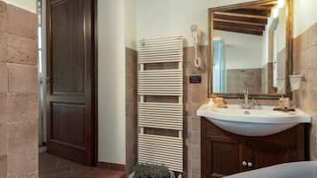 Un baño con puerta de madera, radiador blanco, lavamanos con espejo y una planta pequeña.