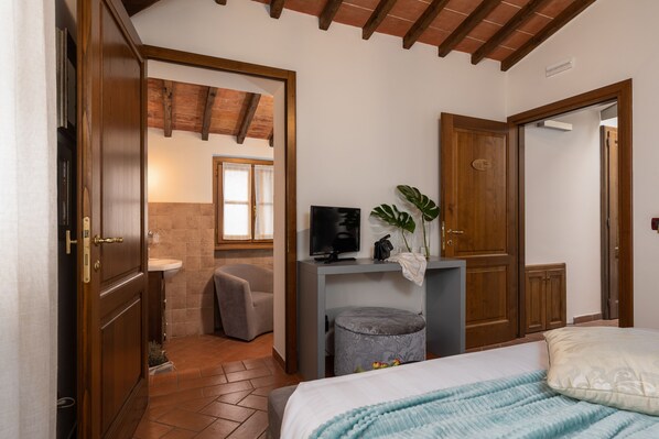 A bedroom with a bed, a bedside table with a TV, a small stool, and a wooden wardrobe.
