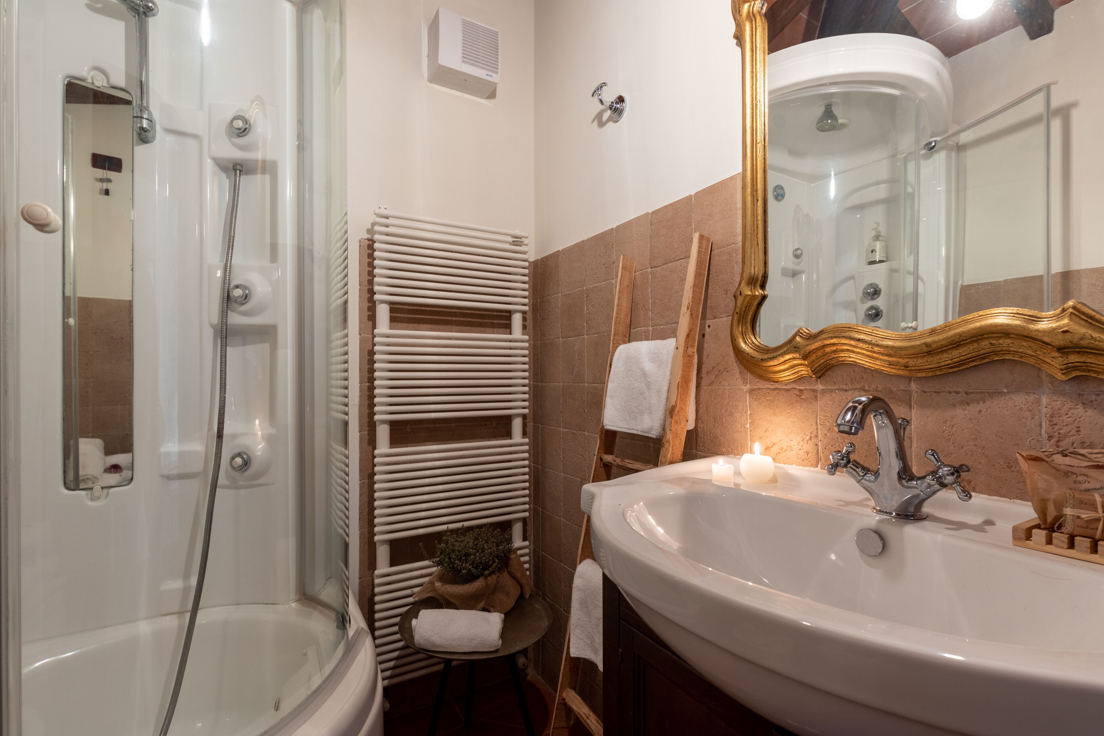 A bathroom with a glass-enclosed shower, a white sink with a gold faucet, and a mirror with a gold frame.